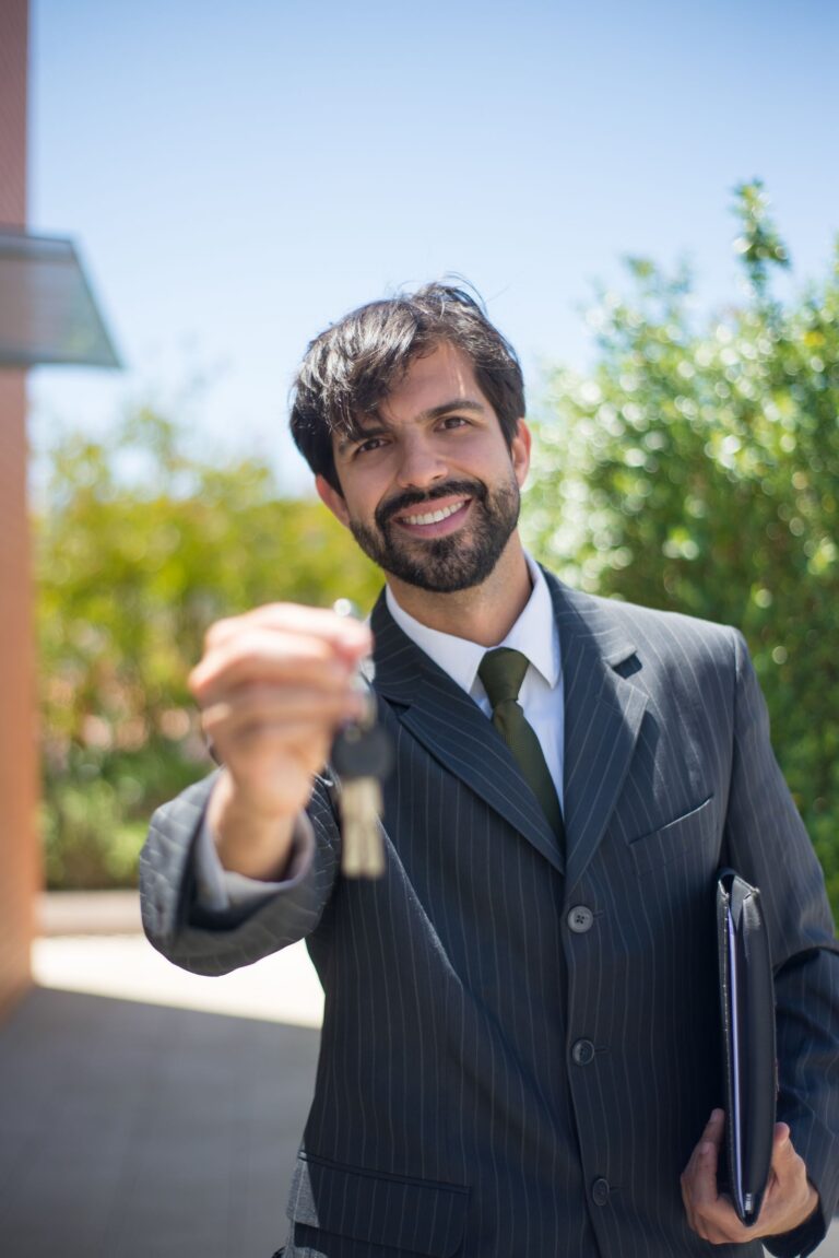 A smiling property manager in a pinstripe suit holding out a set of house keys